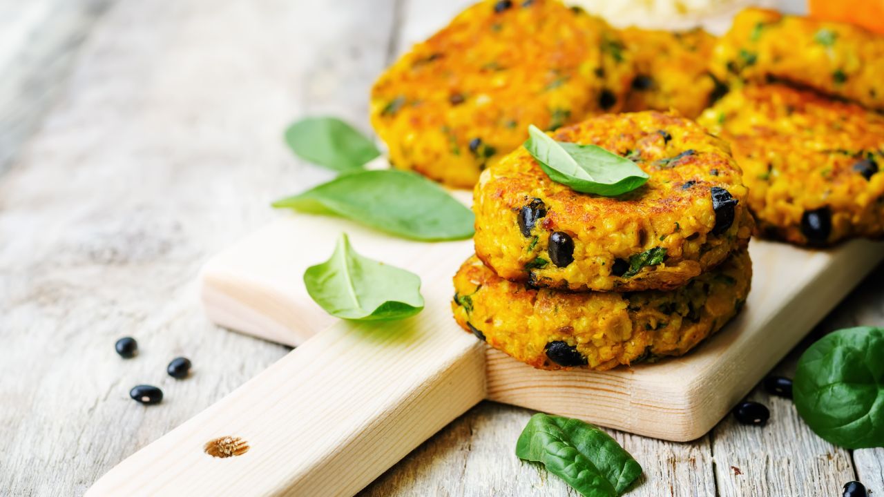 Homemade black bean burger patty stacked with fresh lettuce, tomato, and avocado on a whole grain bun